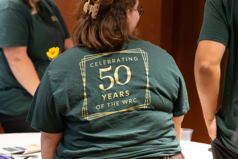 A person wears a green T-shirt with gold lettering celebrating 50 years of the WRC.