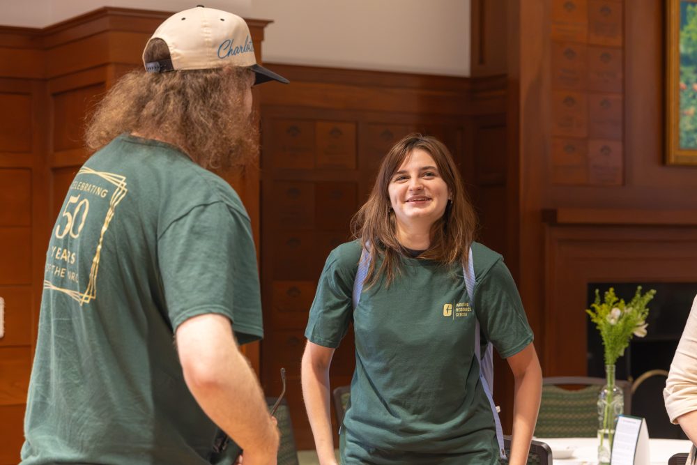 Two individuals in matching green shirts engage in conversation in a wood-paneled room.